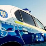 Blue and white police car with a crest on the door and an emergency light on the roof, 'Politia' visible on the side.