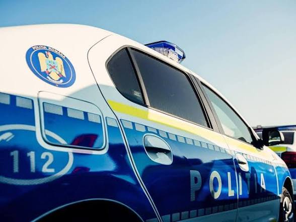 Blue and white police car with a crest on the door and an emergency light on the roof, 'Politia' visible on the side.
