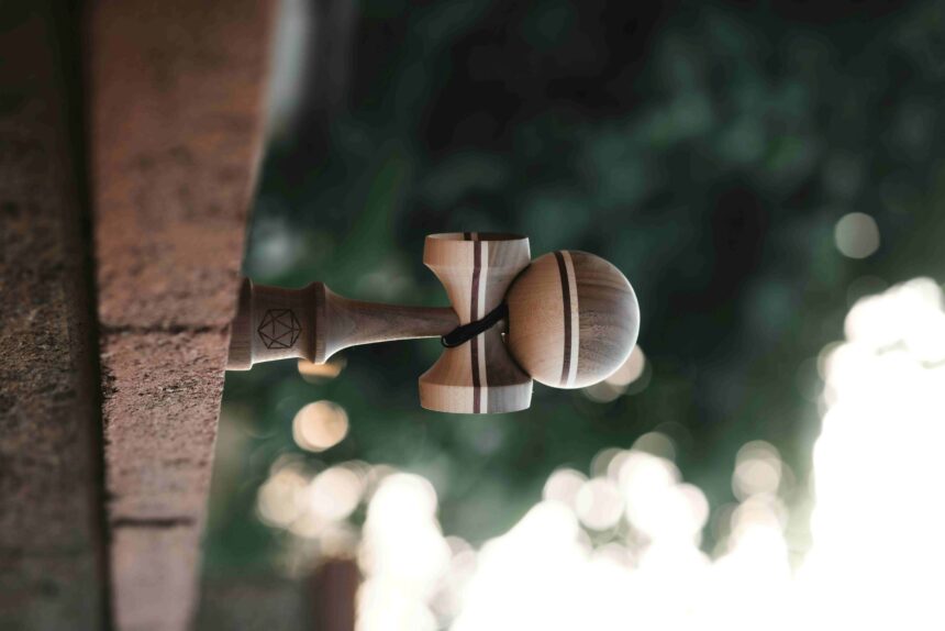 Wooden kendama toy hanging from a rope tied to a wooden post outdoors, with blurred green foliage in the background.