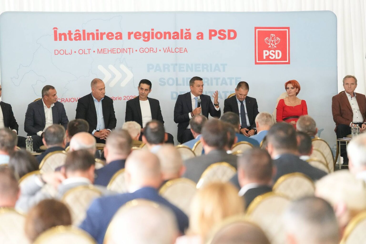 Panel of politicians seated on stage during a conference, backdrop with PSD logo and Romanian text, audience in foreground