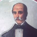 Portrait of a middle-aged man with a white mustache, wearing a dark suit and bow tie, facing forward.
