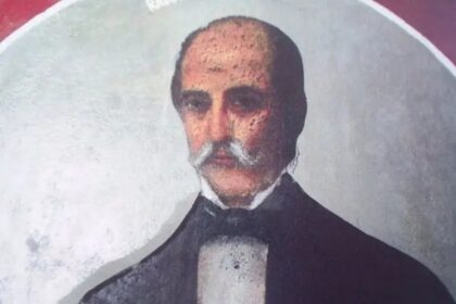 Portrait of a middle-aged man with a white mustache, wearing a dark suit and bow tie, facing forward.