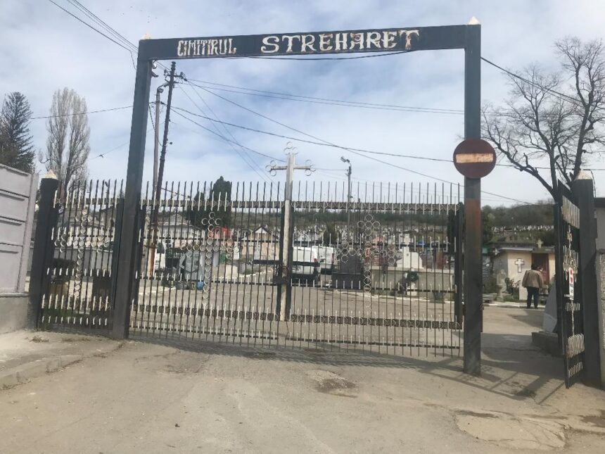 Entrance to a cemetery with a tall wrought-iron gate reading 'Cimitirul Strehaer' and a visible row of grave markers beyond the gate.