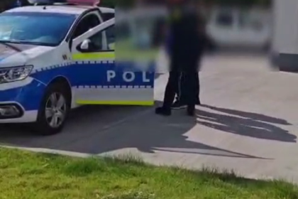 Romanian police car with crest; two officers talk to blurred individuals on a sunny street.