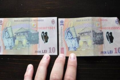 Two ten‑lei Romanian banknotes laid side by side on a dark surface, with a few fingers visible at the bottom.