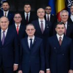 Group of formally dressed officials posing for a photo in front of flags.