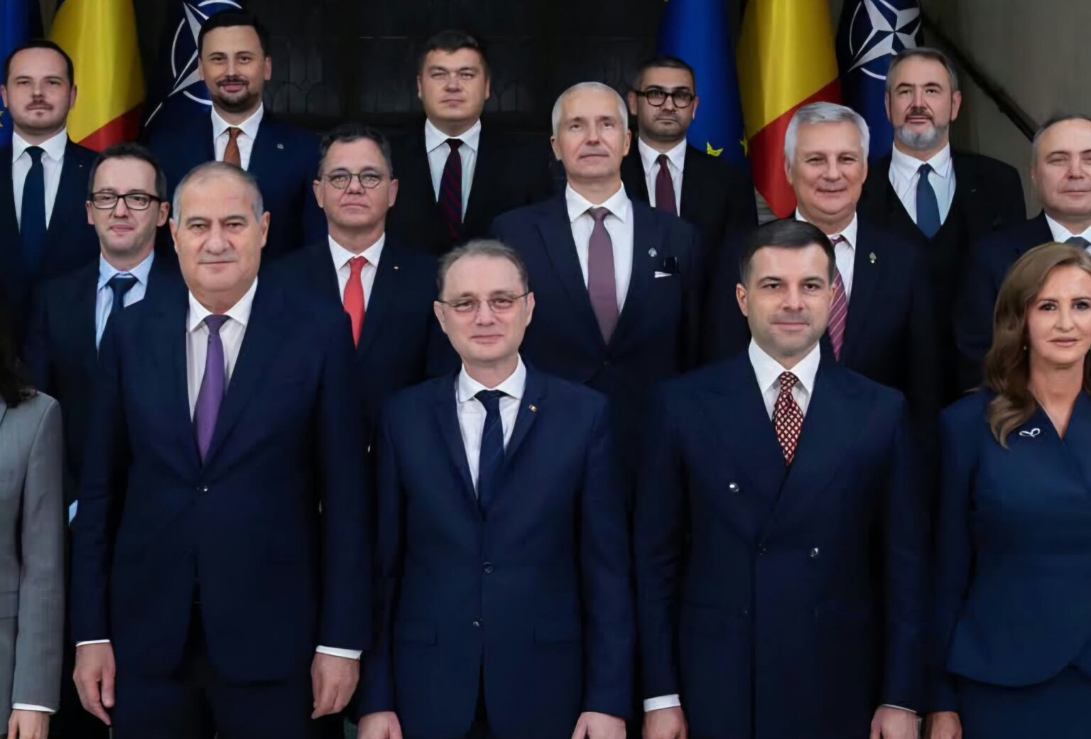 Group of formally dressed officials posing for a photo in front of flags.