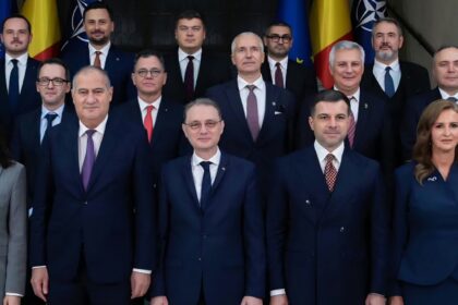 Group of formally dressed officials posing for a photo in front of flags.