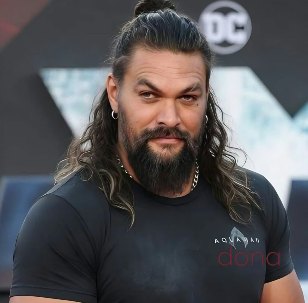 Man with long dark hair tied back and a beard wearing a black T-shirt at a public event.