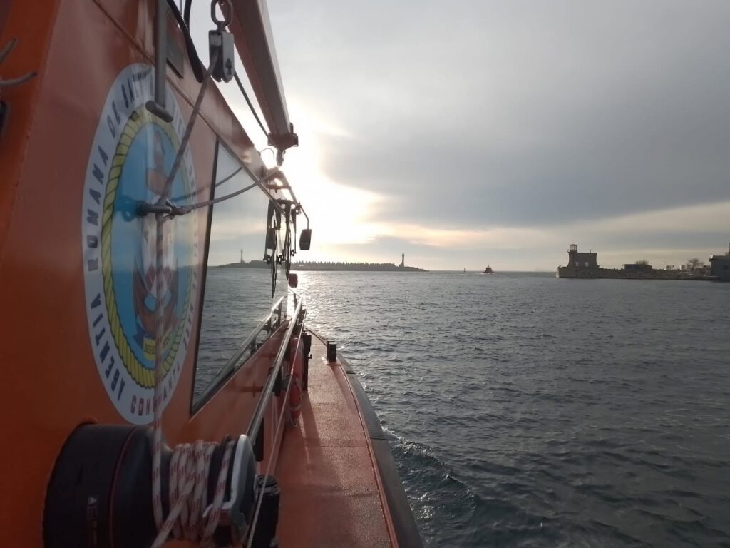 Incident în Marea Neagră: O navă turcească, lovită de dronă. Foto: Facebook - Jurnalul Olteniei – Știri din Craiova și Oltenia Orange rescue boat side view with equipment, sun reflecting on water, harbor and lighthouse in distance.