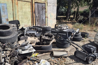 Outdoors, a junkyard scene with tires and car parts scattered on a dirt ground in front of a weathered building, with a Romanian Police logo overlay.