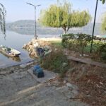 Riverside scene with a small boat tied to a rocky shore and debris scattered along the bank.