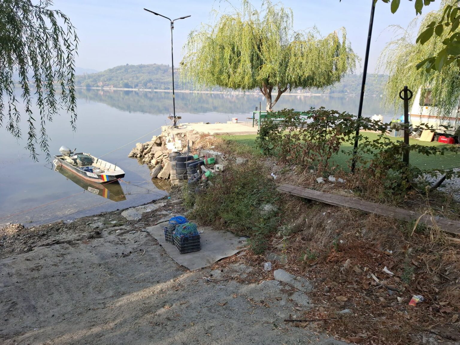 Riverside scene with a small boat tied to a rocky shore and debris scattered along the bank.