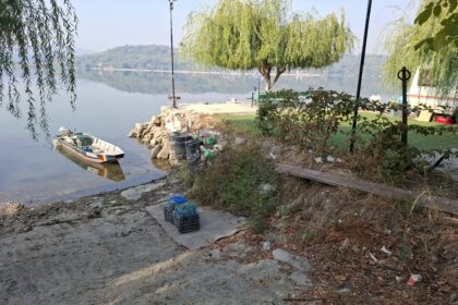 Riverside scene with a small boat tied to a rocky shore and debris scattered along the bank.