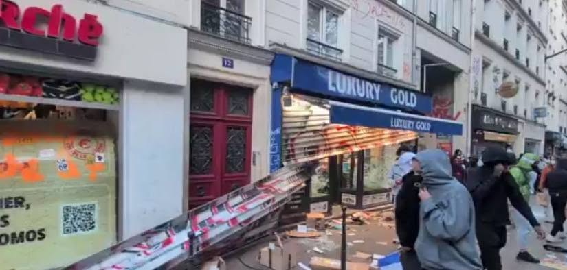 Street scene with shopfronts and police tape cordoning off the area as bystanders look on and debris lie on the ground surface.] , not good