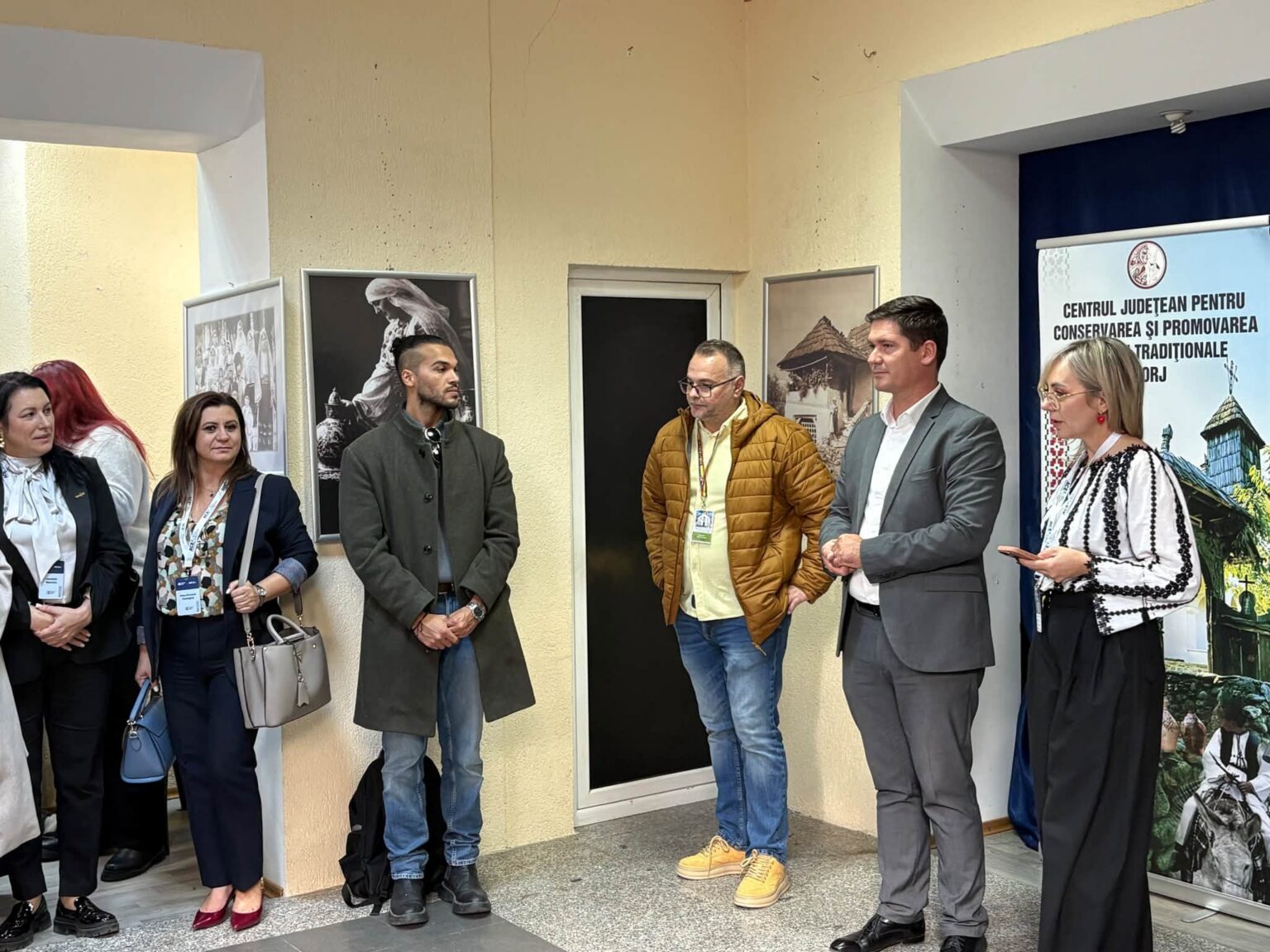 Group of people standing indoors along a wall with framed photos and a banner, as if at an event or briefing.