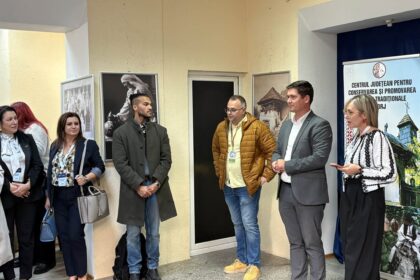 Group of people standing indoors along a wall with framed photos and a banner, as if at an event or briefing.