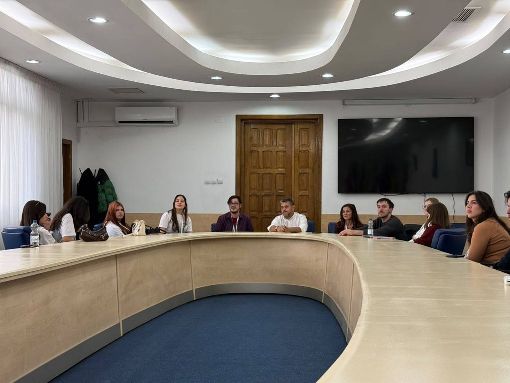 864143178_4615112358808728_5739459112101244977_n - Jurnalul Olteniei – Știri din Craiova și Oltenia Group of people seated around a curved conference table in a modern meeting room, listening to a discussion.