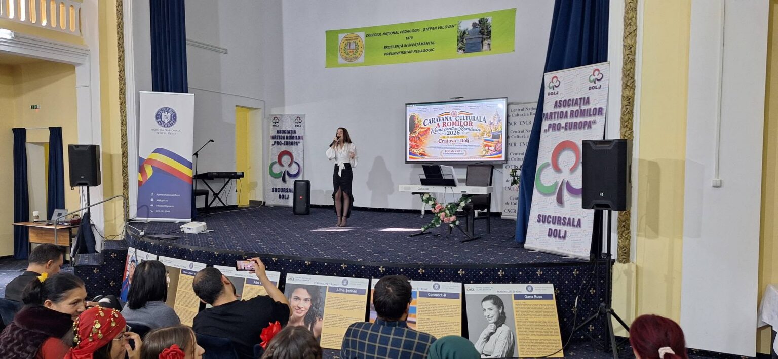 Caravana Culturală a Romilor a ajuns la Craiova - Jurnalul Olteniei – Știri din Craiova și Oltenia Female singer in a white blouse and black skirt performing on a stage with a large screen displaying an event banner behind her