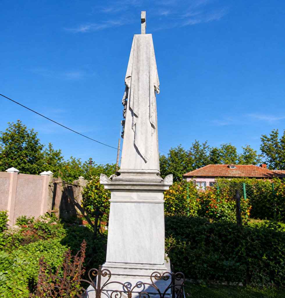 Marble obelisk monument wrapped in draped fabric in a garden under a bright blue sky, enclosed by decorative fencing.