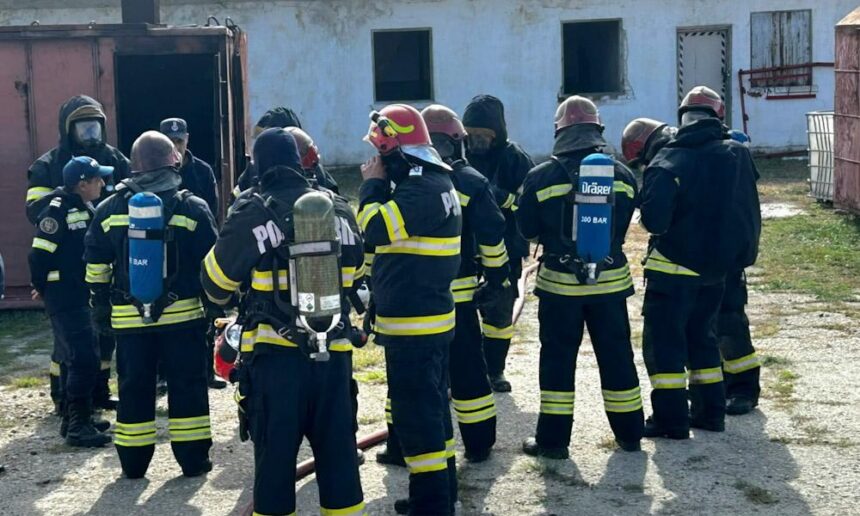 Group of firefighters in turnout gear with air tanks standing in a circle outside a building, likely during a drill or briefing.