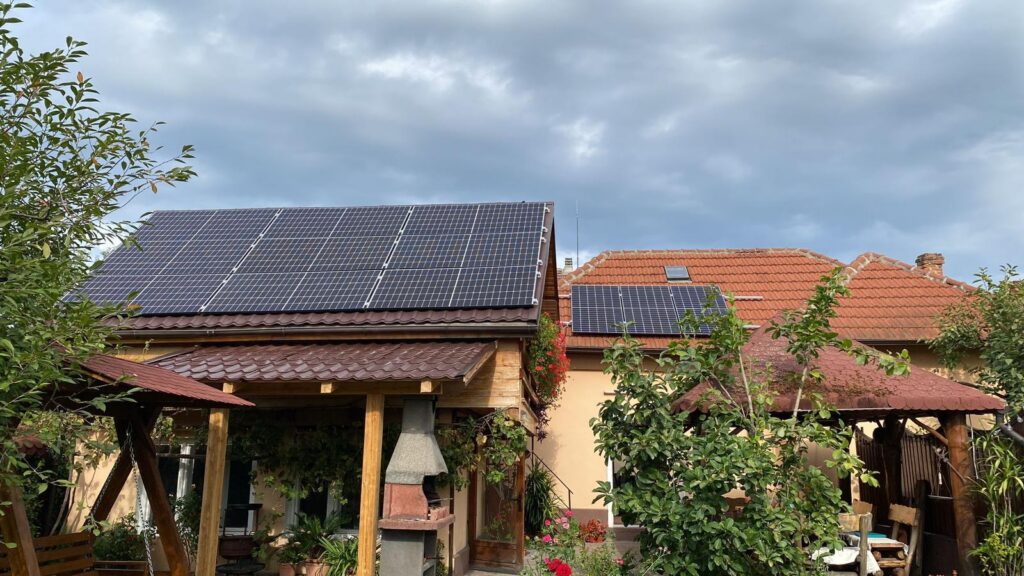 Two houses with solar panels on their red-tiled roofs in a green garden setting.