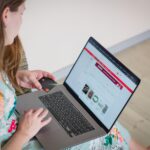 Person holding a credit card while using a laptop to browse an online shopping site on a bright screen.