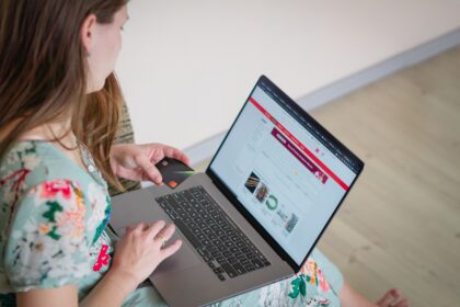 Person holding a credit card while using a laptop to browse an online shopping site on a bright screen.