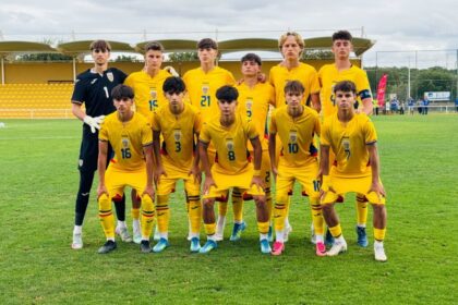 Youth soccer team in yellow uniforms posing for a group photo on a grassy field, with a goalkeeper in black on the left.