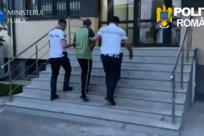 Three plainclothes officers escort a man up the building stairs outside a government facility, with police logos visible at top corners (Romania).