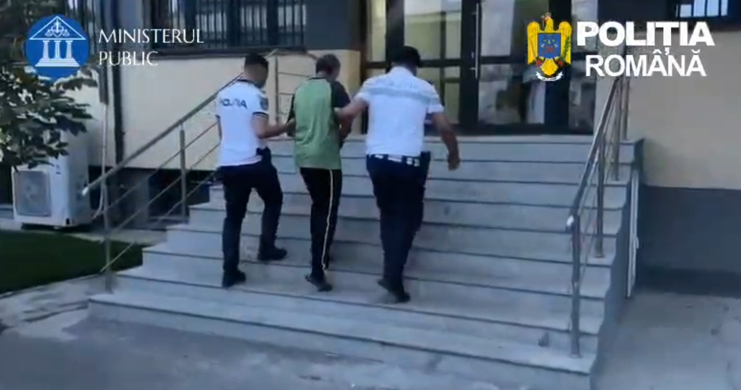 Three plainclothes officers escort a man up the building stairs outside a government facility, with police logos visible at top corners (Romania).