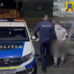 Nighttime street scene of Romanian police detaining a handcuffed suspect, with officers and a marked POLITIA car nearby.