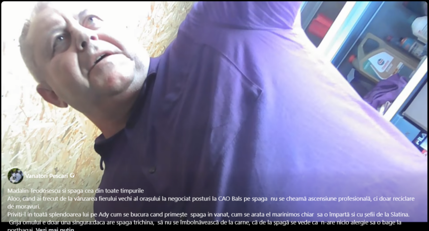 Man in a purple shirt leaning toward the camera in a workshop or shop, shelves with cleaning products visible in the background.