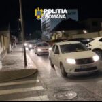 Nighttime street scene with several cars driving in a line, police emblem 'Poliția Română' overlaid at the top left.