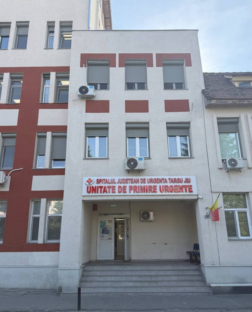 Facade of a hospital building with a red-and-beige pattern; sign above entrance reads 'Unitate de Primire Urgente' (Emergency Department) in Romanian.
