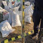 Pile of white sandbags around a cordoned-off area with police cars in the background.