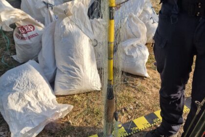 Pile of white sandbags around a cordoned-off area with police cars in the background.