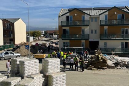 Construction site in a residential area with workers and stacked building materials in front of a three-story building complex.
