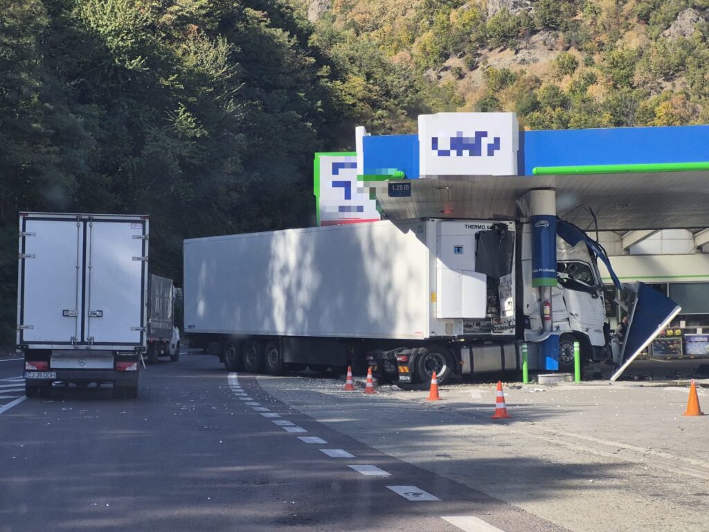 WhatsApp Image 2026-10-06 at 135321 - Jurnalul Olteniei – Știri din Craiova și Oltenia Gas station fueling area with two large white trucks and orange cones, forested hillside in the background.
