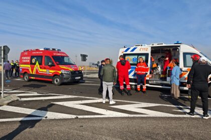 Group of emergency responders and bystanders beside two ambulances on a road under a clear blue sky on scene