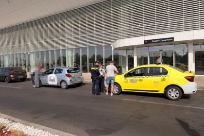 Airport curb scene with a yellow taxi and a light blue hatchback as police speak with a man outside the departures entrance.