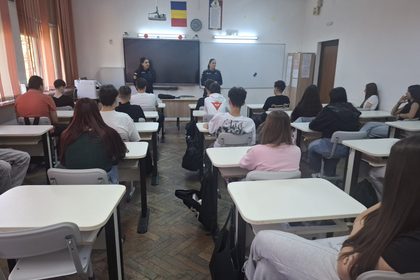 Classroom filled with students watching two police officers speak at the front near a whiteboard and a hanging projector.