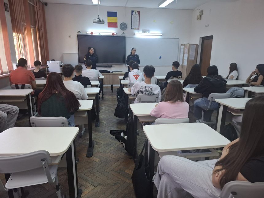 Classroom filled with students watching two police officers speak at the front near a whiteboard and a hanging projector.