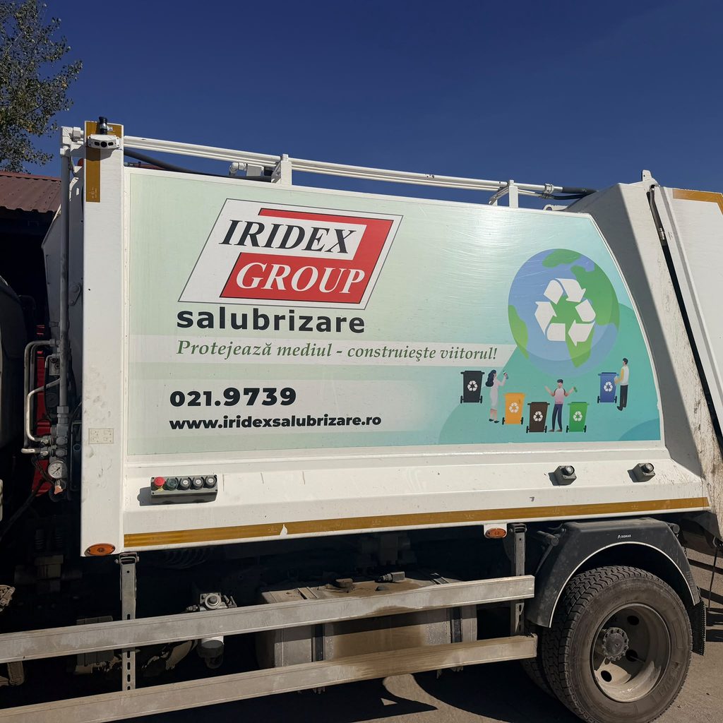 WhatsApp Image 2026-10-08 at 124912 - Jurnalul Olteniei – Știri din Craiova și Oltenia Side of a white truck trailer with a large Iridex Group sign and a circular recycling graphic, blue sky above.