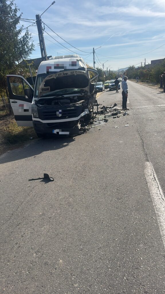 White delivery van heavily damaged at the front, hood open, debris scattered on a rural road, onlookers nearby.