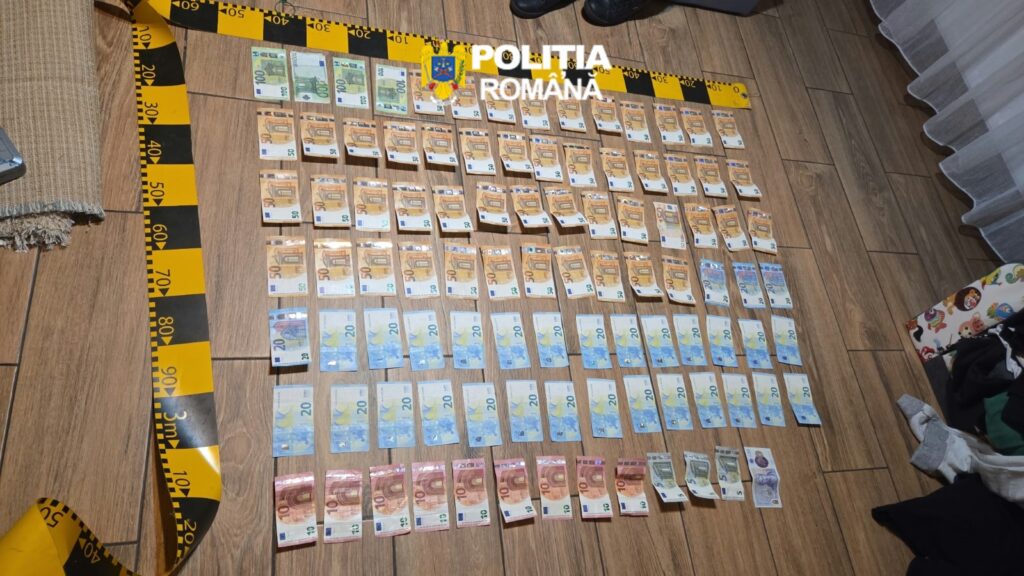 Bundles of euro banknotes neatly laid out on a wooden floor beside yellow-and-black police tape reading POLITIA ROMANA, suggesting seized cash evidence.