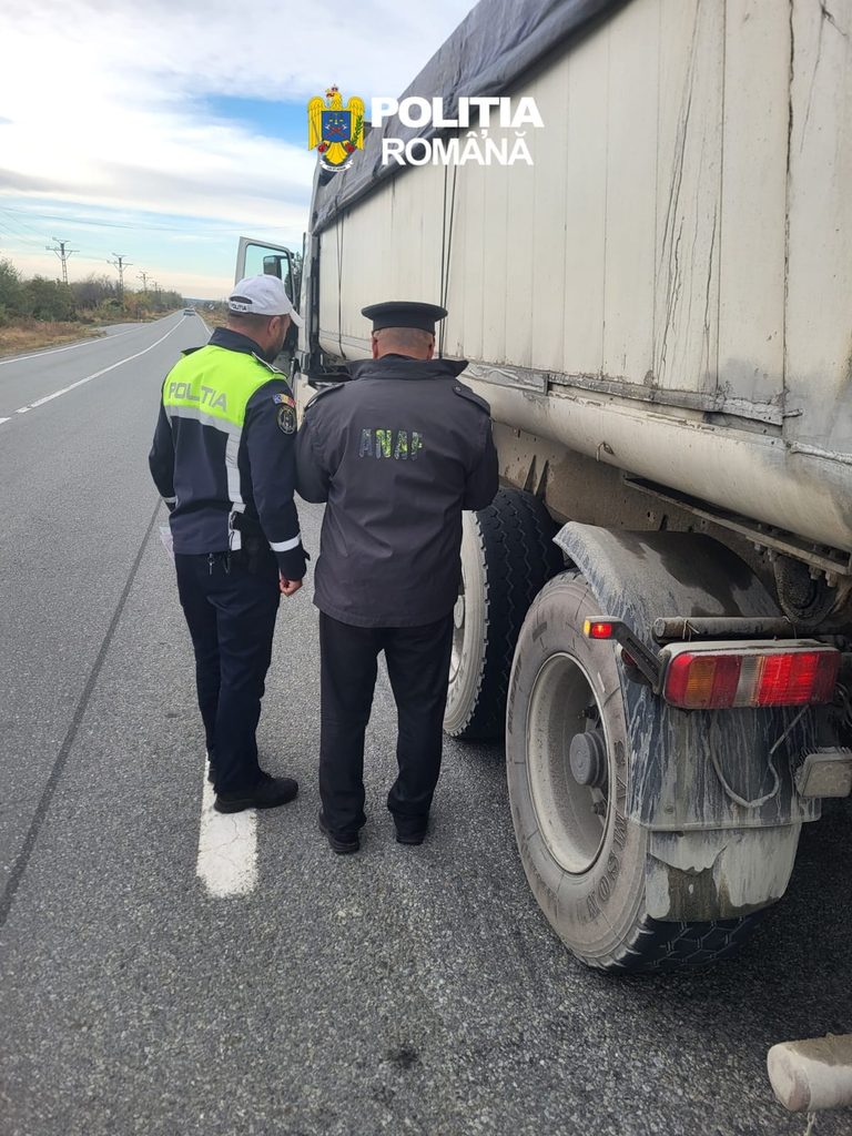 Two Romanian police officers inspect the side of a large truck on a highway shoulder.