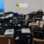 Room filled with stacks of folded clothes and numerous handbags laid out on tables, police emblem 'Politia Romana' on the wall above.