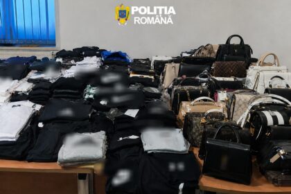 Room filled with stacks of folded clothes and numerous handbags laid out on tables, police emblem 'Politia Romana' on the wall above.