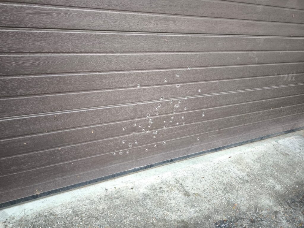 WhatsApp Image 2026-10-22 at 152108 - Jurnalul Olteniei – Știri din Craiova și Oltenia Brown corrugated metal garage door with a cluster of soap bubbles attached near the center-bottom area.